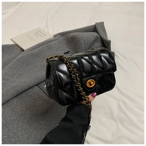 Détail macro du sac bandoulière noir matelassé avec chaîne dorée et fermoir rotatif chic