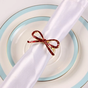 Detail of red enamel bow napkin ring on white fabric with golden metallic edges