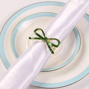 Detail of green enamel bow napkin ring with gold trim on white silk napkin