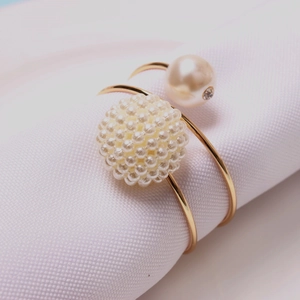 Elegant gold napkin ring with white pearl cluster and rhinestone accent on white fabric