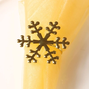 Close-up of golden snowflake napkin ring with polished metallic finish on a yellow cloth