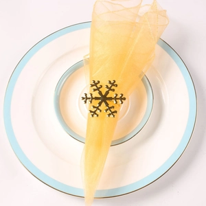 Detailed top view of golden metal snowflake napkin ring with yellow mesh napkin on plate