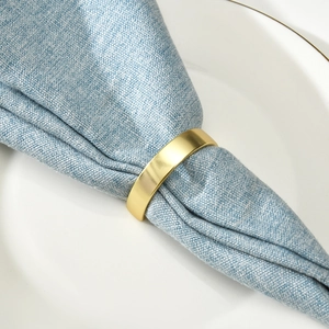 Rond de serviette doré mat sur serviette en lin bleu clair et assiette blanche