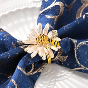 Rond de serviette doré élégant avec marguerite et abeille en cristal sur nappe bleue