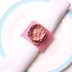 Rond de serviette en toile rose avec fleur en tissu brun sur assiette blanche