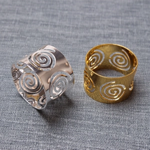 Close-up of hollow swirl metal napkin rings in gold and silver finishes on grey fabric