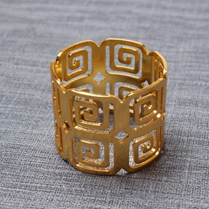 Golden napkin ring with geometric spiral hollow pattern on a gray textured background