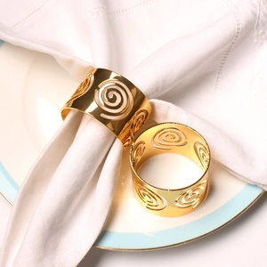 Elegant gold metal napkin rings with hollow swirl design on white napkins and ceramic plates