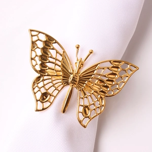 Detailed close-up of a gold-plated hollow butterfly napkin ring on a white napkin cloth