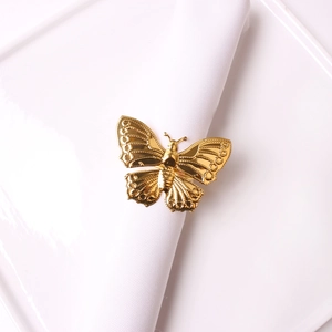 Detailed view of hollow gold butterfly napkin ring with embossed patterns on white fabric