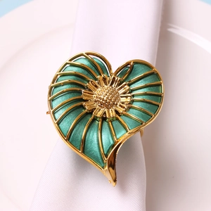 Detail view of a green heart-shaped napkin ring with golden floral center on a white cloth