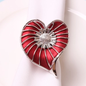 Close-up of a silver heart napkin ring with red enamel and pearl texture on white fabric