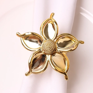 Elegant gold five-petal flower napkin ring with textured center on a white fabric napkin
