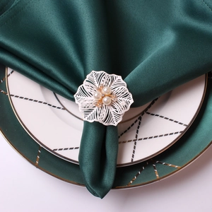 Elegant white floral napkin ring with pearls and rhinestones on dark green fabric