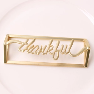 Macro shot of gold 'thankful' metal napkin ring on a light pink porcelain plate