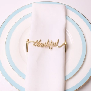 Golden thankful script metal napkin ring placed on white linen for elegant table setting