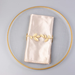 Macro view of gold leaf shaped metal napkin ring on silk napkin and textured plate