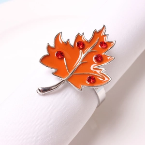 Orange maple leaf napkin ring with enamel finish and red rhinestones on white cloth