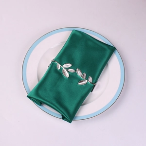 Detail of silver leaf napkin ring and dark green satin fabric on white porcelain plate
