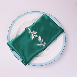 Close-up of a silver leaf napkin ring on a dark green satin napkin over a ceramic plate