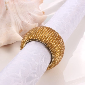 Close-up of golden beaded napkin ring with intricate woven craftsmanship on white linen