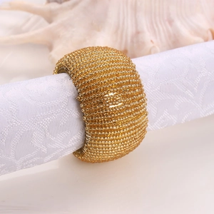 Handcrafted golden beaded napkin rings set on white napkin with seashell decoration