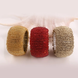 Handcrafted beaded napkin rings in gold, red and silver displayed with a seashell