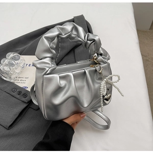 Silver ruched crossbody bag with pearl bow and heart charms on a grey suit backdrop