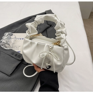 Detail of white pleated cloud bag featuring pearl bow charm and golden metal hardware