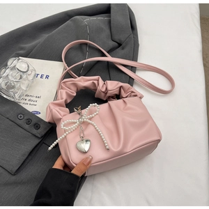 Pink pleated cloud handbag with pearl bow and silver heart pendant on white bedding