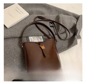 Détail d'un sac seau en cuir marron foncé avec boucle en métal sur un fond de manteau gris