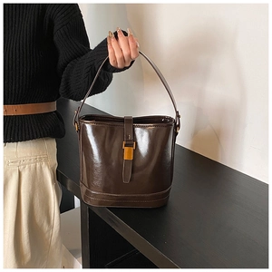 Vue détaillée du sac seau marron foncé avec boucle en métal doré et texture cuir brillante