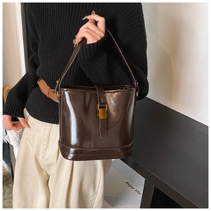 Détail d'un sac seau en cuir verni marron foncé avec boucle dorée et bandoulière