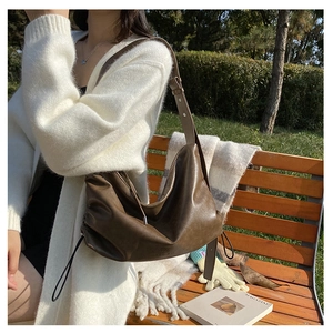 Detail of vintage dark brown faux leather hobo bag with drawstring on a park bench
