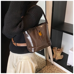 Sac seau en cuir verni marron foncé avec fermoir doré porté dans un style urbain chic