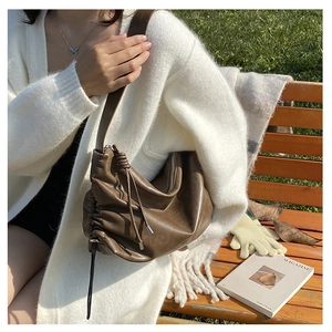 Close-up of dark brown pleated leather crossbody bag with drawstring side detail