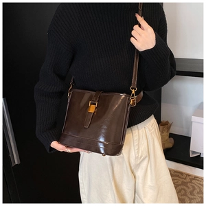 Détail du sac seau marron foncé brillant avec boucles dorées porté par un mannequin