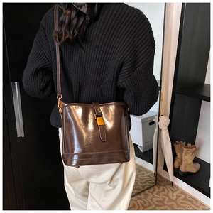 Détail d'un sac seau marron foncé brillant avec boucle dorée porté par un modèle