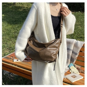 Detailed view of a brown soft leather crossbody bag on a model in an outdoor autumn setting