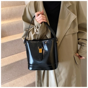Détail d'un sac seau en cuir noir brillant avec un fermoir en métal doré poli et une poignée