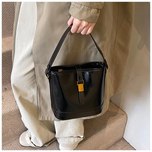 Détail d'un sac seau en cuir noir brillant vintage avec boucle dorée sur escalier