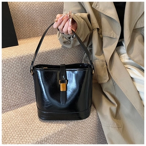 Gros plan sur un sac seau en cuir noir brillant avec boucle dorée et longue anse