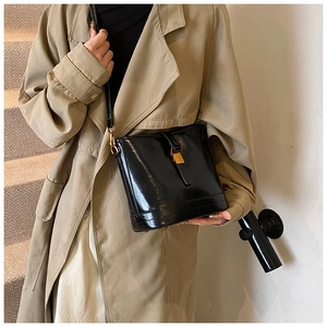 Détail d'un sac seau noir en cuir verni avec fermoir doré sur un trench-coat beige classique