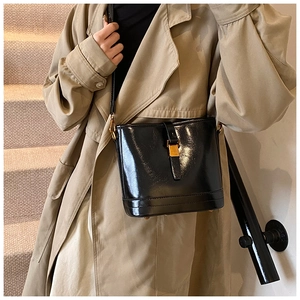 Détail du sac seau en cuir verni noir avec boucle dorée et bandoulière réglable