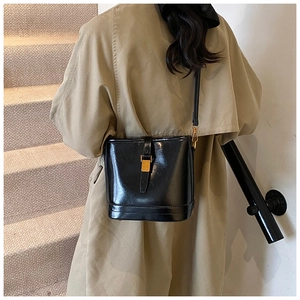 Sac seau en cuir noir avec boucle en métal porté avec un trench-coat kaki dans l'escalier