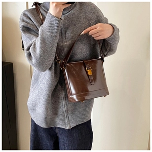 Détail d'un sac seau en cuir marron brillant avec boucle dorée sur pull gris