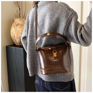 Détail du sac seau en cuir marron foncé brillant avec boucle dorée et bandoulière