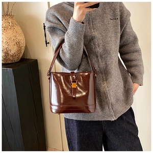 Vue latérale du sac seau marron foncé brillant avec fermoir doré sur pull