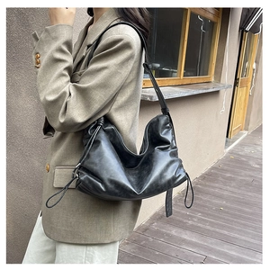 Detail of black faux leather shoulder bag featuring knotted strap and pleated cloud design