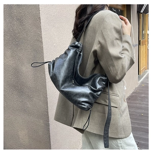 Detailed side view of a black pleated leather shoulder bag worn by a model in a corridor